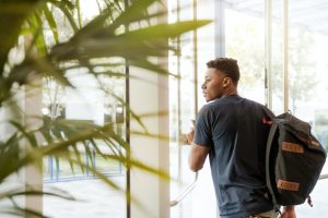 male student walking with backpack out of a building